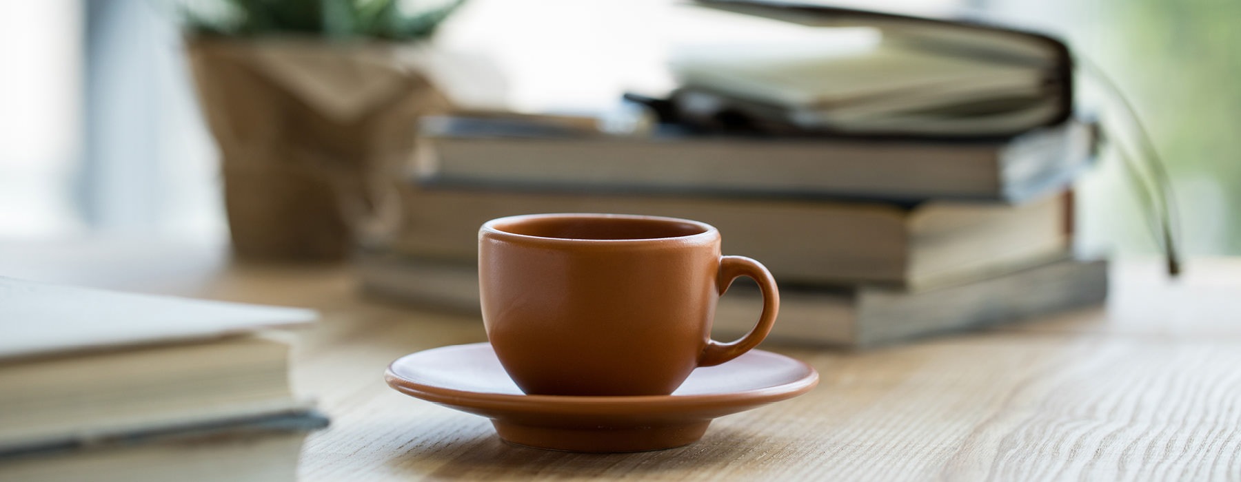 a cup of coffee on a table with books and potted plant